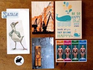5 bunte Kunst- und Postkarten aus Hamburg schön angeordnet auf einem Holztisch.